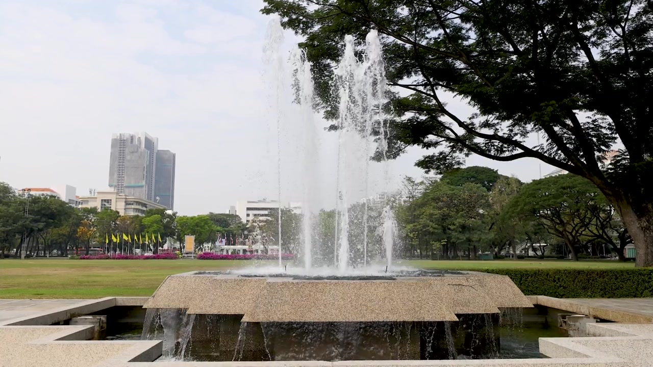 Plano general estático de una fuente de piedra de varios niveles rociando agua en un parque exuberante