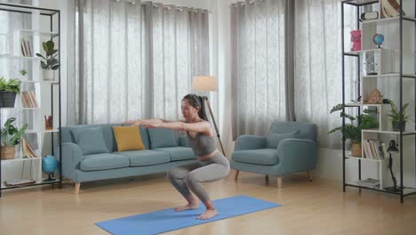 joven mujer atlética asiática en ropa deportiva practicando la postura de la silla en la alfombra en casa