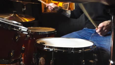 gorgeous static slow motion footage of a man playing acoustic drums and hitting bronze and orange colored shiny drum cymbals next to him. the man has tattoos and is playing in a well lit studio room.