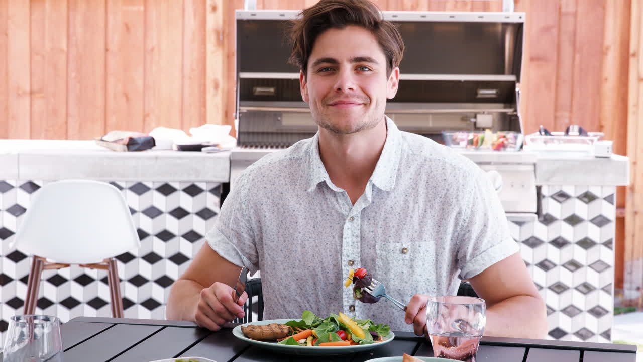 joven blanco comiendo almuerzo en una mesa en el jardín