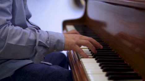 talented elderly piano artist musician is playing classical music wearing blue shirt and jeans close up hands moody cinematic scene slow motion