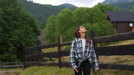 mujer en una camisa a cuadros en una valla de madera en un paisaje de montaña