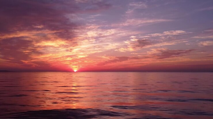 A Breathtaking Sunset Over Calm Waters: Nature's Vibrant Palette of Colors Reflected in the Tranquil Ocean at Dusk, Creating a Serene and Peaceful Atmosphere