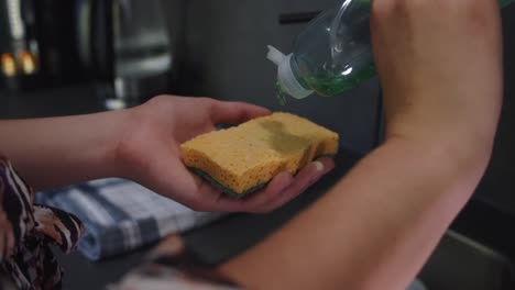 mujer puso líquido para lavar platos en una esponja en la cocina