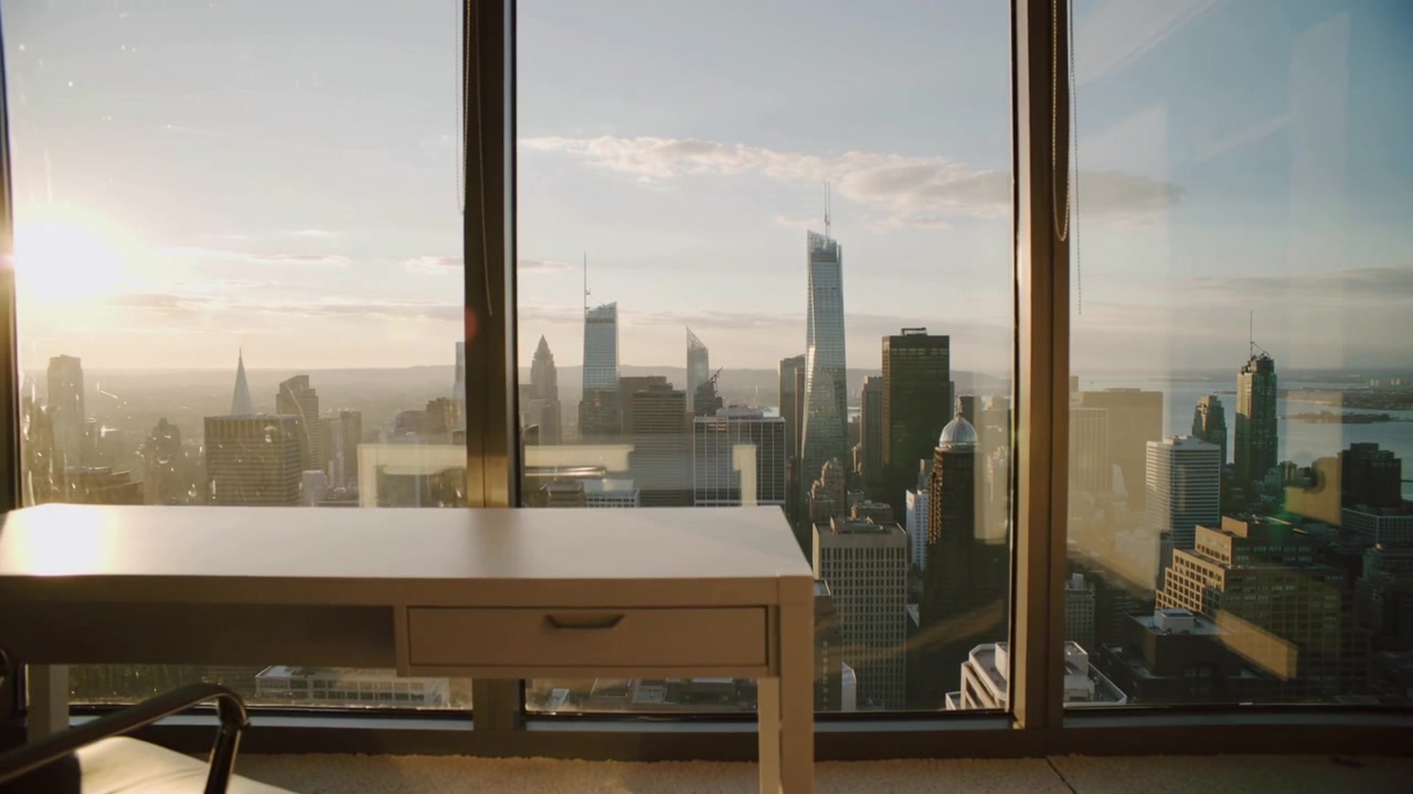 Panoramica della telecamera che si sposta a destra e si allontana in un ufficio ai piani alti, rivelando una scrivania, una sedia e lo skyline.