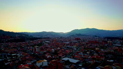 Noche-Con-Cielo-Amarillo-Claro-Entre-La-Montaña-Con-Un-Vuelo-Cenital-Desde-Una-Vista-De-Drones-Sobre-Los-Techos-Rojos-De-Las-Casas-De-La-Pequeña-Ciudad