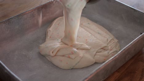 funfetti cake batter being poured into a flour lined metal cake pan in 4k 60fps