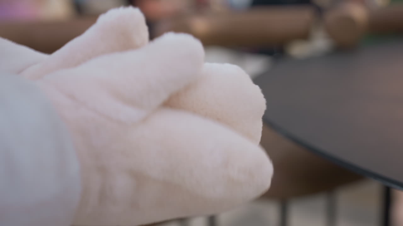 Close-up of hands clapping together in soft, plush winter gloves, the blurred background with indistinct figures adds depth, making it perfect for winter fashion