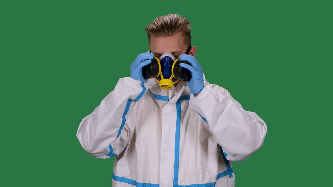 retrato de un virólogo masculino en un traje de protección blanco y guantes quirúrgicos pone y luego quita el respirador médico. pantalla verde, llave de croma. cámara lenta