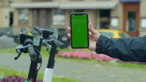 young man paying for electric scooter use app with green mock-up screen smartphone. green screen smartphone.