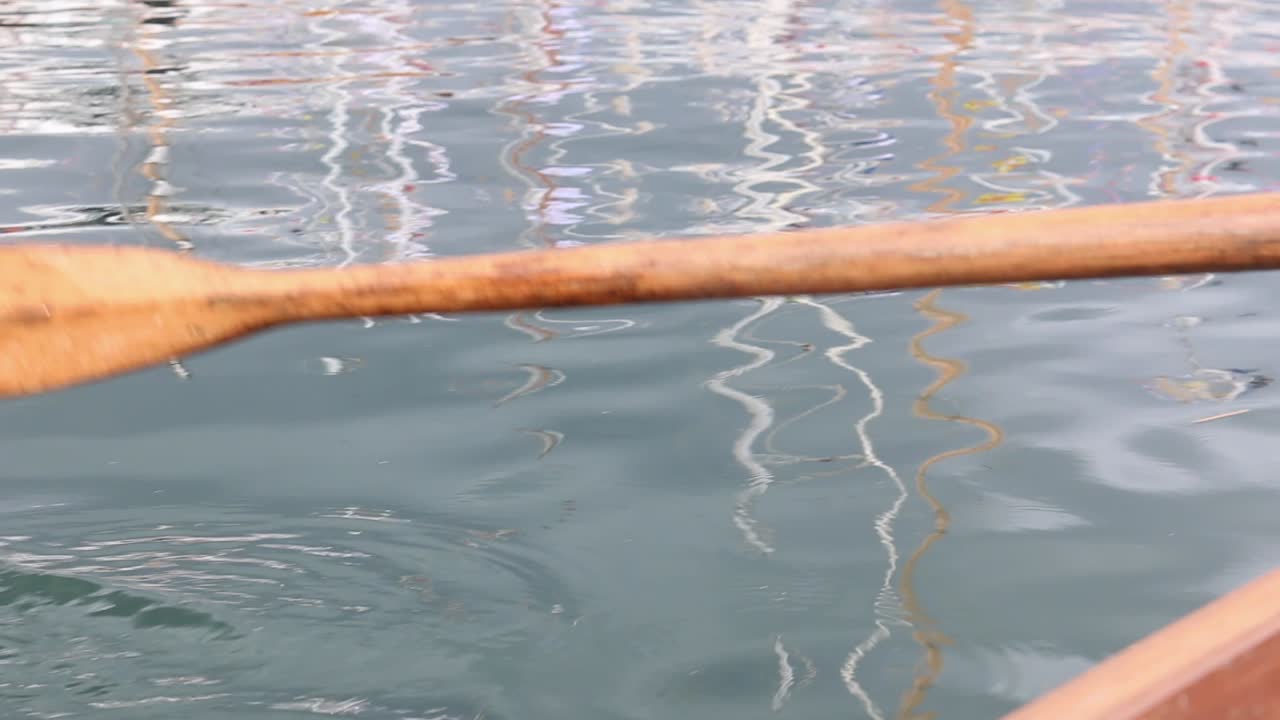 Wooden oar over side of boat paddling through blue ocean water causing ripples
