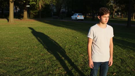 a young person standing in a sunlit park, casting a long shadow on the grass, portraying a moment of reflection amidst nature's calmness