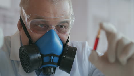 extreme close-up of a scientist in a blue respirator and protective glasses a developer of a coronavirus vaccine holding a red ampoule. the doctor looks at the new vaccine. a new type of virus medicine. high quality 4k footage