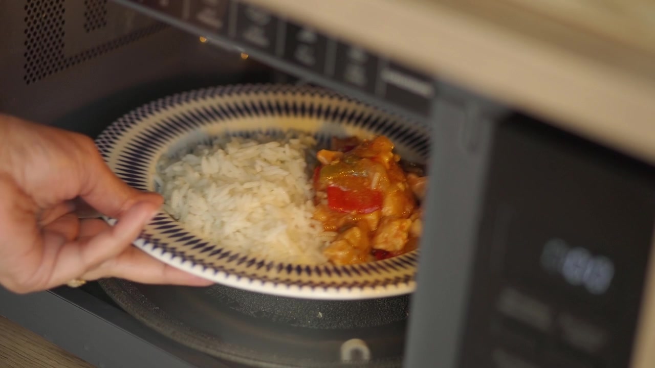 Mano che toglie un piatto di cibo dal microonde