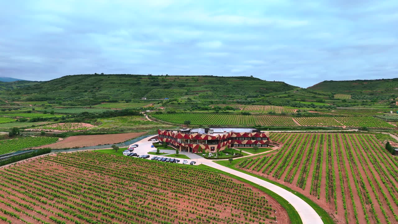 Lateral aerial shot of a modern winery and extensive vineyards in La Rioja, Spain. Scenic viticultural landscape with hills and cultivated fields. Captured at low altitude