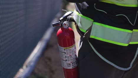 primed fire extinguisher hanging from the hi-viz vest of a public work with a chain link fence in the background