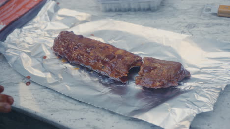 manos agregando salsa marinada a las costillas a la barbacoa antes de envolverlas en papel de aluminio listo para cocinar