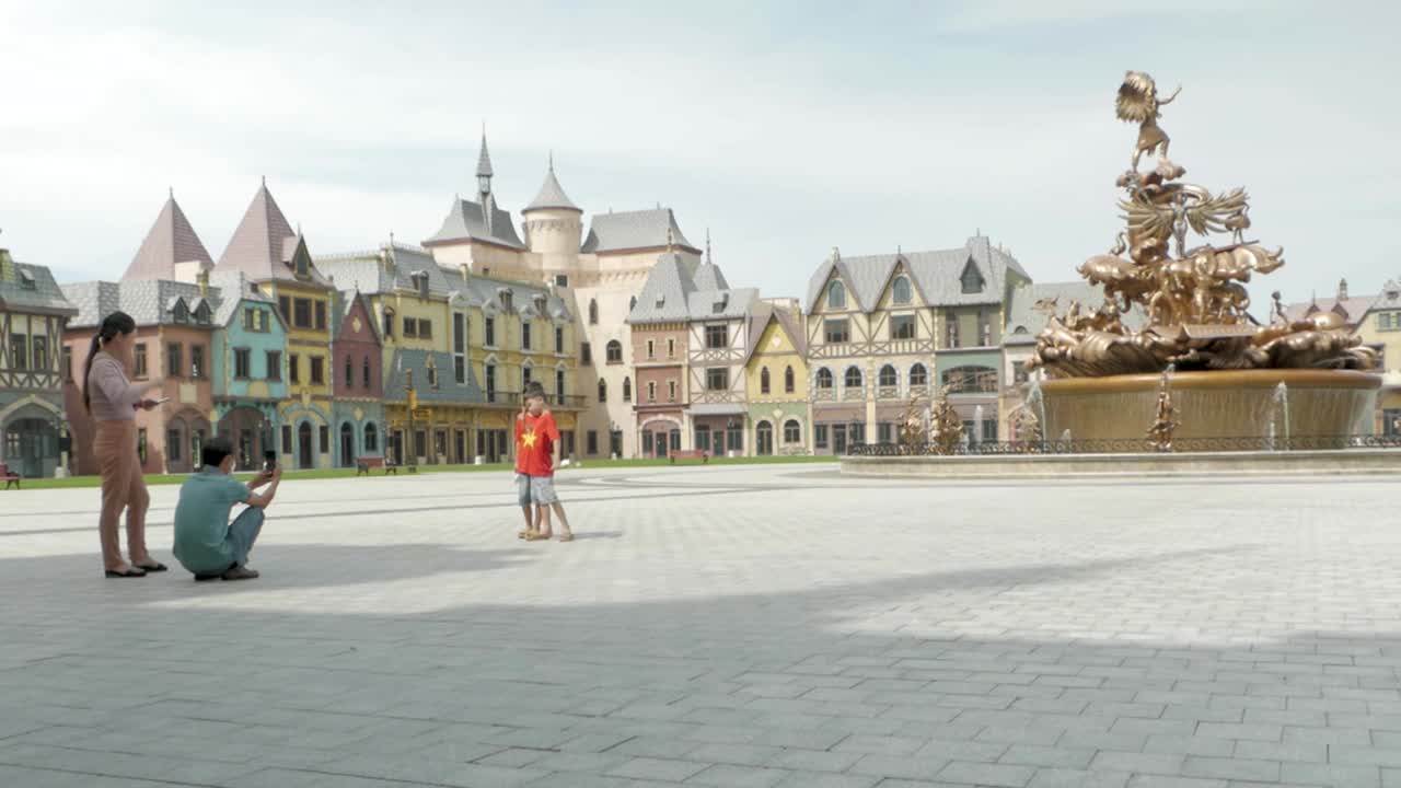 A family enjoys posing for photos in front of a grand fountain in a colorful European-style square