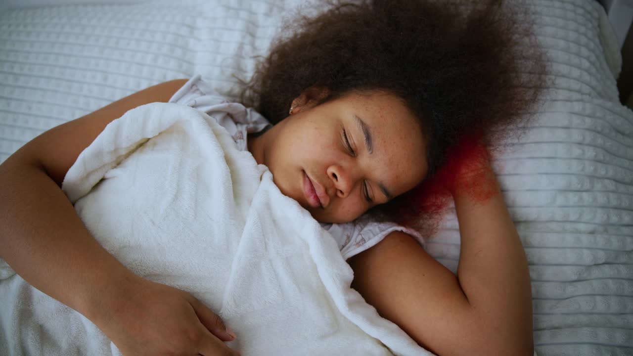 Peaceful young black woman lying comfortably in bed, experiencing deep relaxation through restful sleep and dreaming moments during quiet nighttime hours