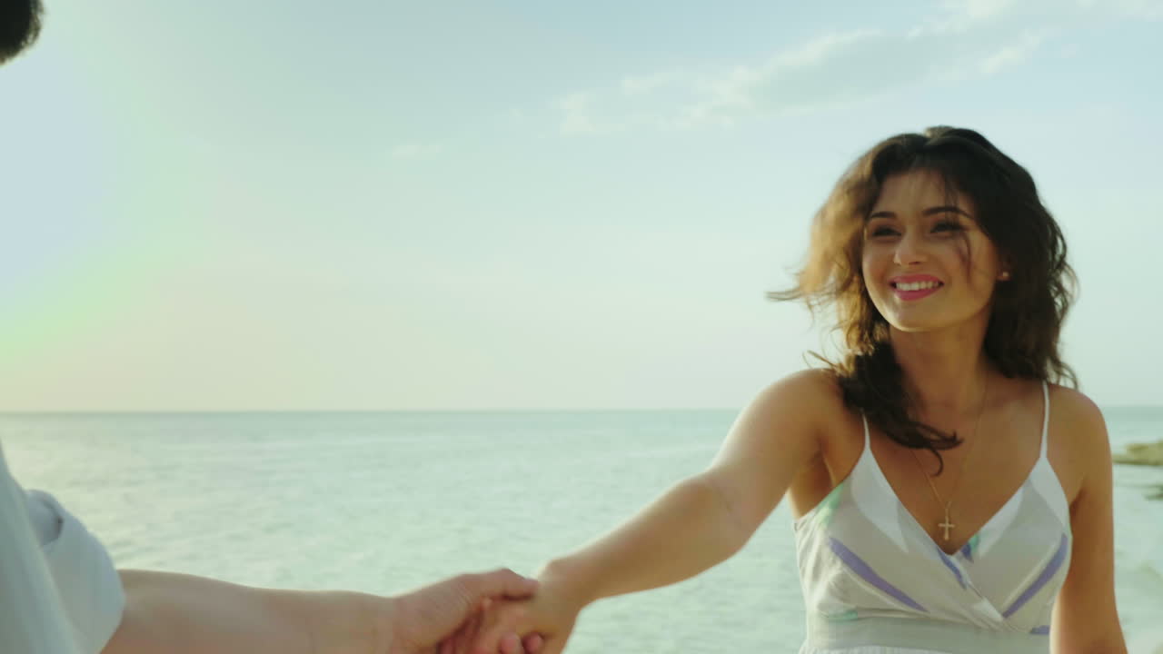 mujer joven conduce detrás de sí misma retrato va a lo largo de la playa sonrisas cabello croa en el viento pov vi