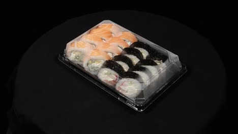 sushi rolls rotates in a plastic container on a black background. meal delivery