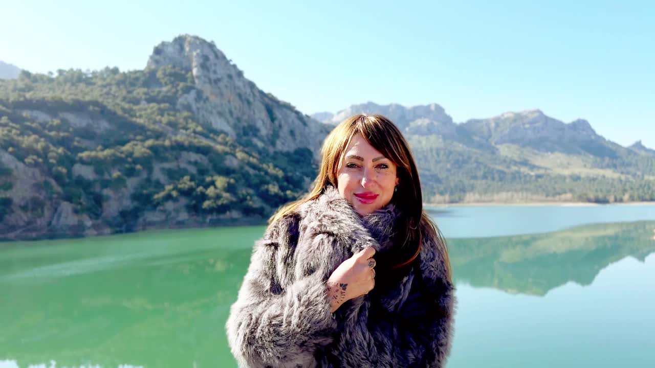 Turkuaz bir dağ gölünün kenarında duran kürk mantolu güzel kadın.