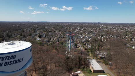 An-aerial-view-of-a-new-water-tower-with-another-in-the-process-of-being-dismantled,-on-a-sunny-day-on-Long-Island,-New-York