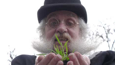 older man with beard looking down at fresh grass growing in his hands