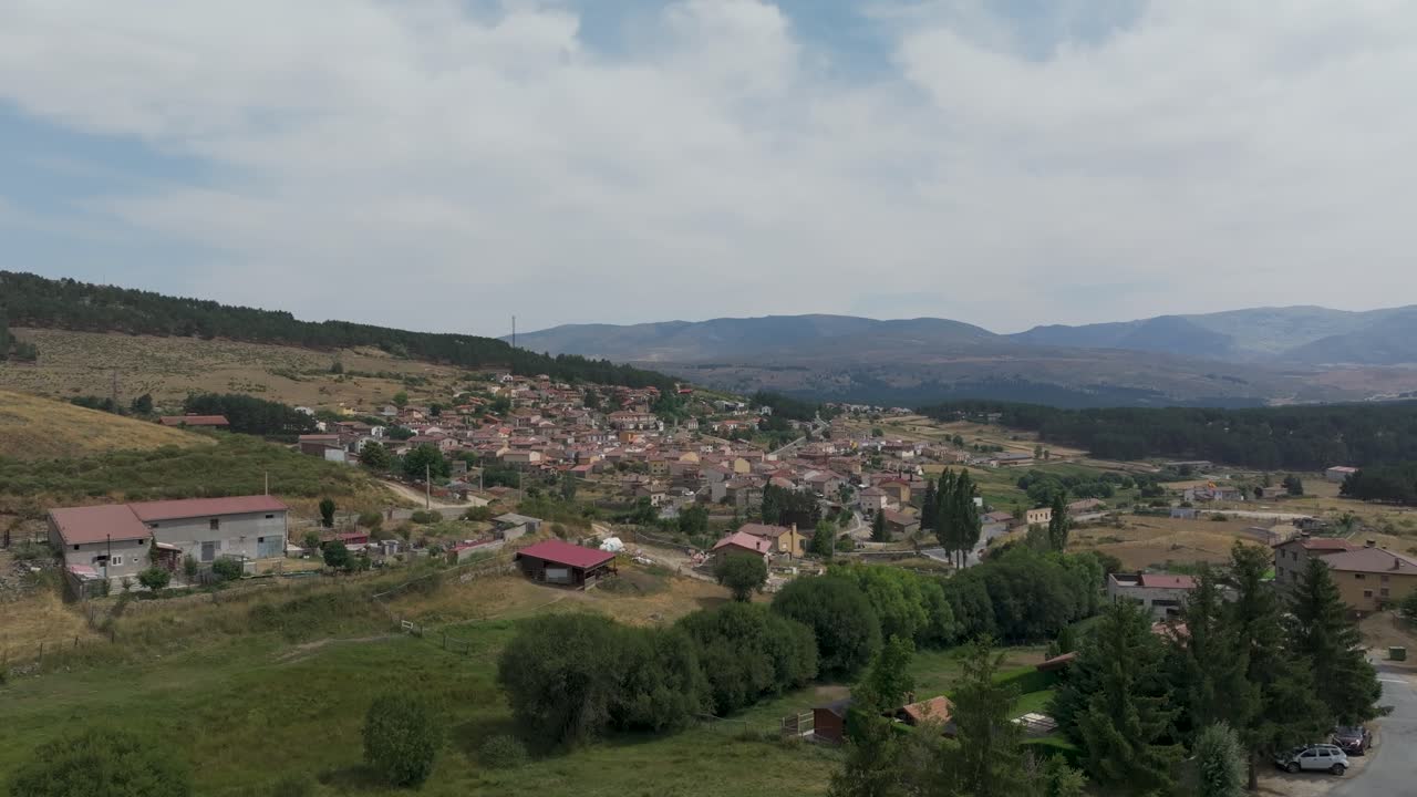 vuelo ascendente con un dron de la ciudad de avila de hoyo del espino desde su periferia, se encuentra en una ladera y apreciamos sus alrededores con un fondo de la cordillera de gredos