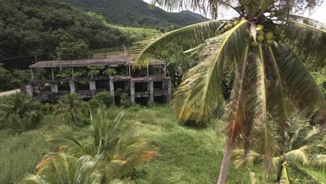 Aerial-dolly-shot-of-derelict-tropical-resort-building-on-a-tropical-island-with-palm-trees