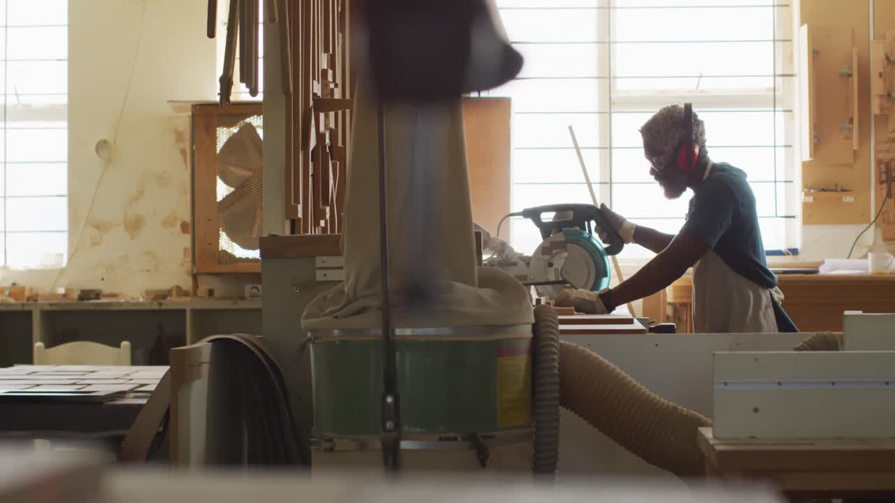 carpintero afroamericano cortando tablas de madera con una sierra eléctrica en una carpintería