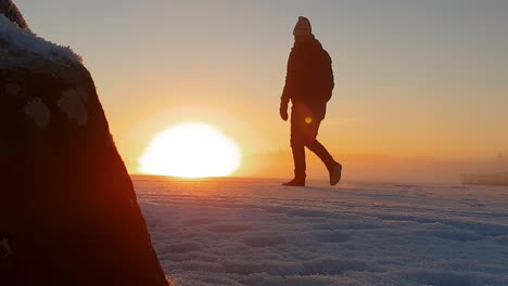 athletic male walking off on frozen lake in snowy winter landscape, golden sunset in arctic climate