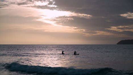 two women rowing sitting on paddleboards against sunset over the sea