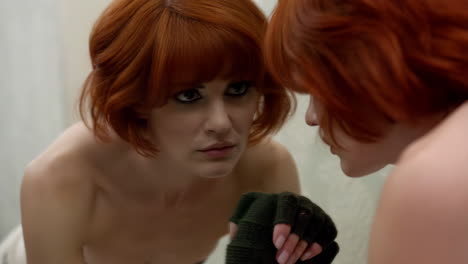 woman with red hair looking intently into mirror