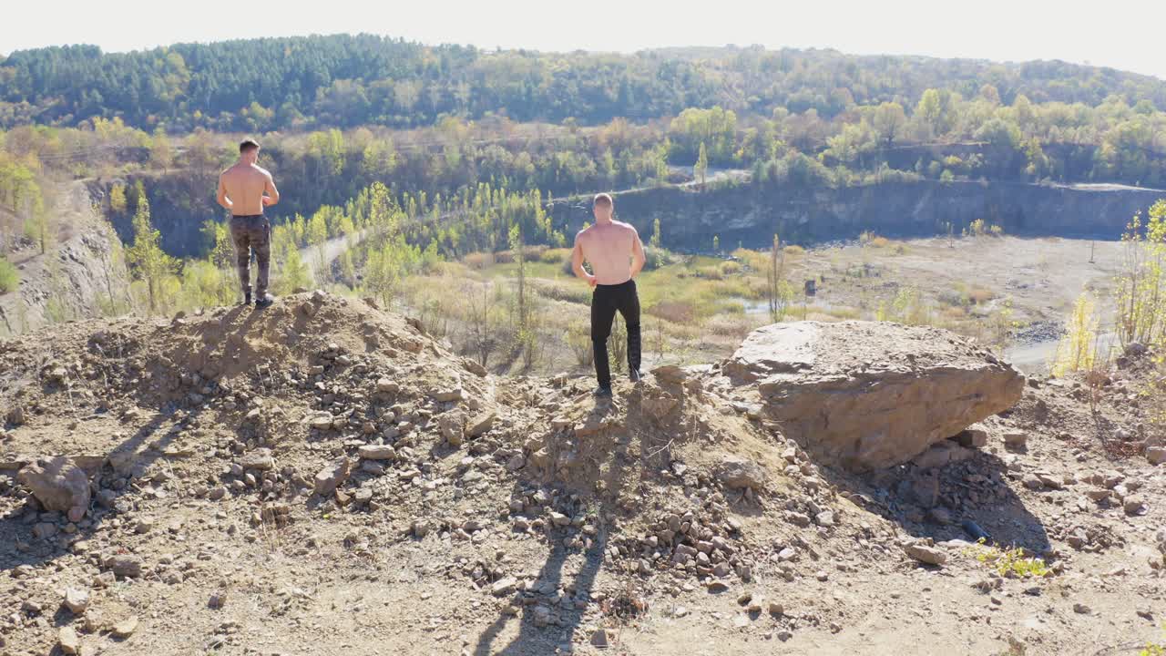 Back view of athletic men running. Active sportsmen without shirt show their trained body standing at the edge of a hill. Aerial view.