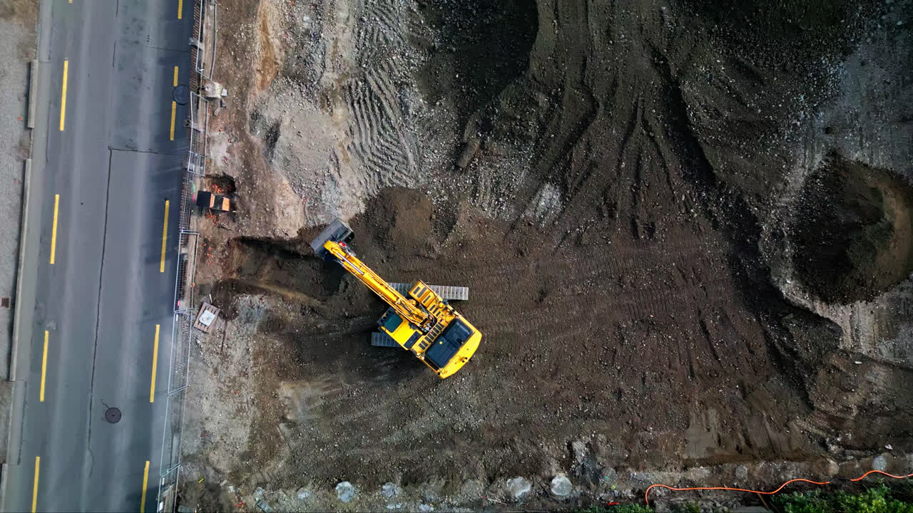el avión no tripulado desciende de arriba hacia abajo en la excavadora eliminando la suciedad húmeda del sitio de construcción