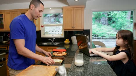 father preparing food while daughter using laptop in kitchen 4k