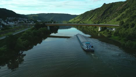 barge traversing a river under a bridge in a green valley