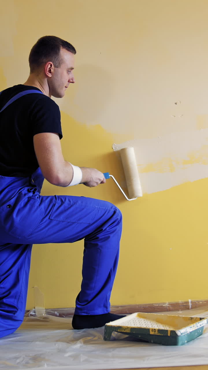 Young man painting wall with roller brush while renovating his apartment. Repair, building and home concept. Vertical video