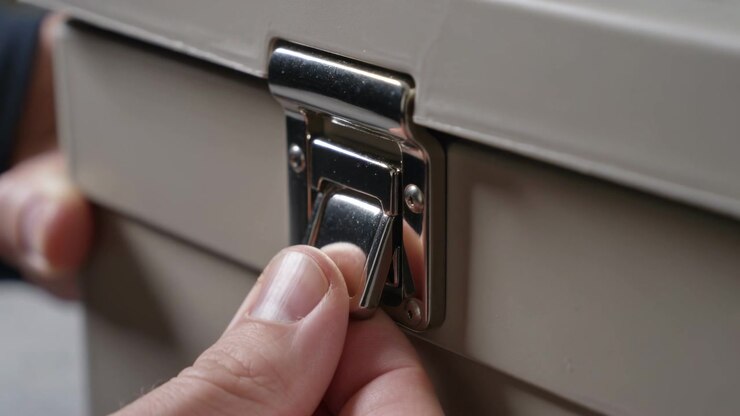 Approaching fingers pinching and lifting tab on beige box, dark-sleeved arm holding, opening case