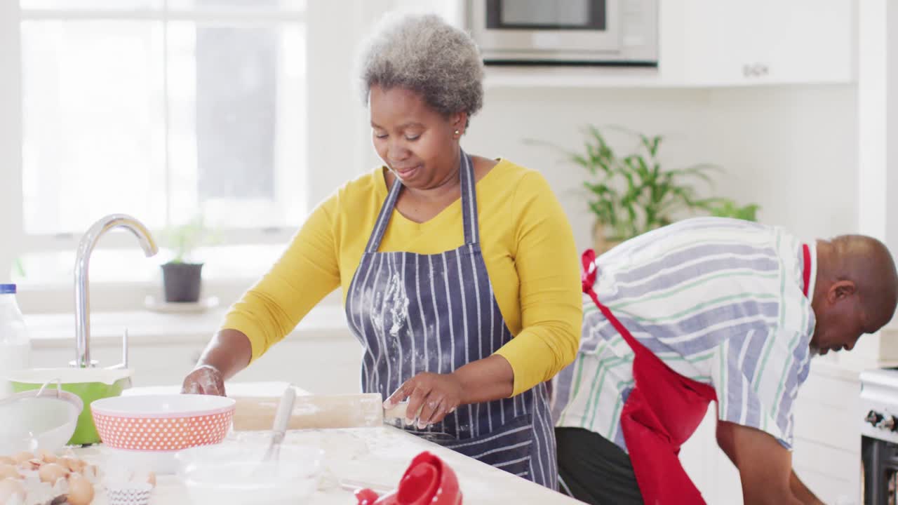 Happy african american senior couple baking together in kitchen, slow motion