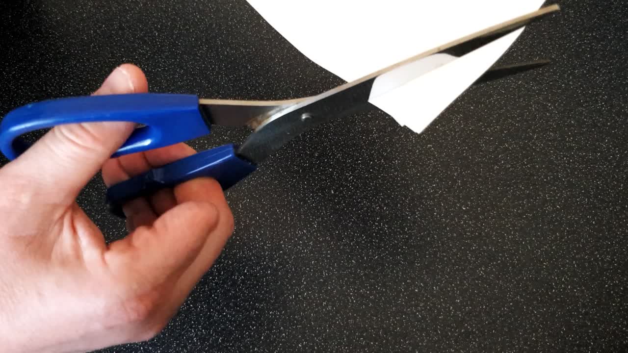 Male with a partially amputated index finger on his right hand cutting strips of white paper diagonally with a pair of blue handled scissor#orrs