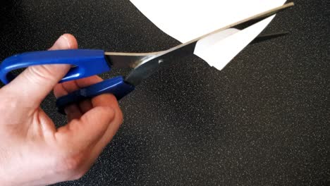 male with a partially amputated index finger on his right hand cutting strips of white paper diagonally with a pair of blue handled scissor#orrs