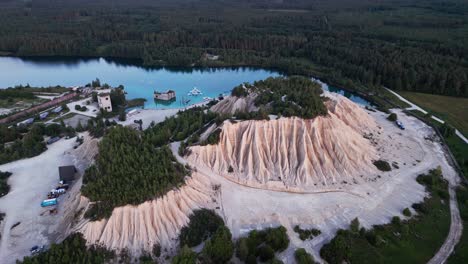 aerial drone view of rummu quarry estonia displays flooded prison ruins turquoise lake water ash hills and pine forest creating a dramatic and unforgettable travel destination