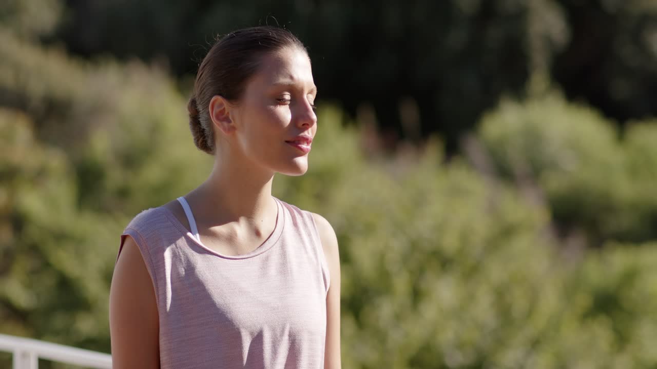 Mujer afroamericana levantando el rostro hacia la luz del sol en una terraza, con una blusa rosa, sintiendo calor
