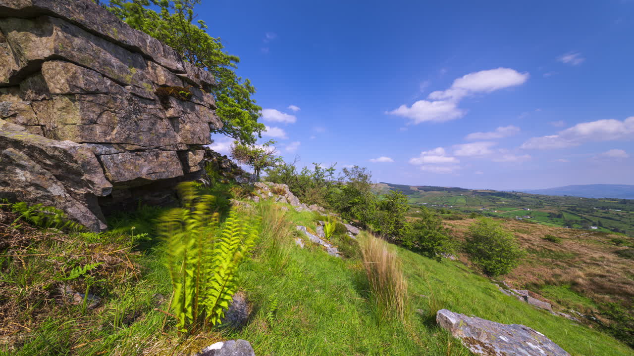 Time lapse of rural landscape with foreground of rocks and grass on hillside with trees and lake in the distance on a spring sunny day in Arigna mountains in county Leitrim in Ireland