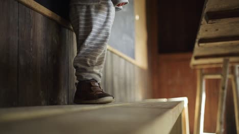 toddler boy stands on wooden bench in hut, feet low angle, no face