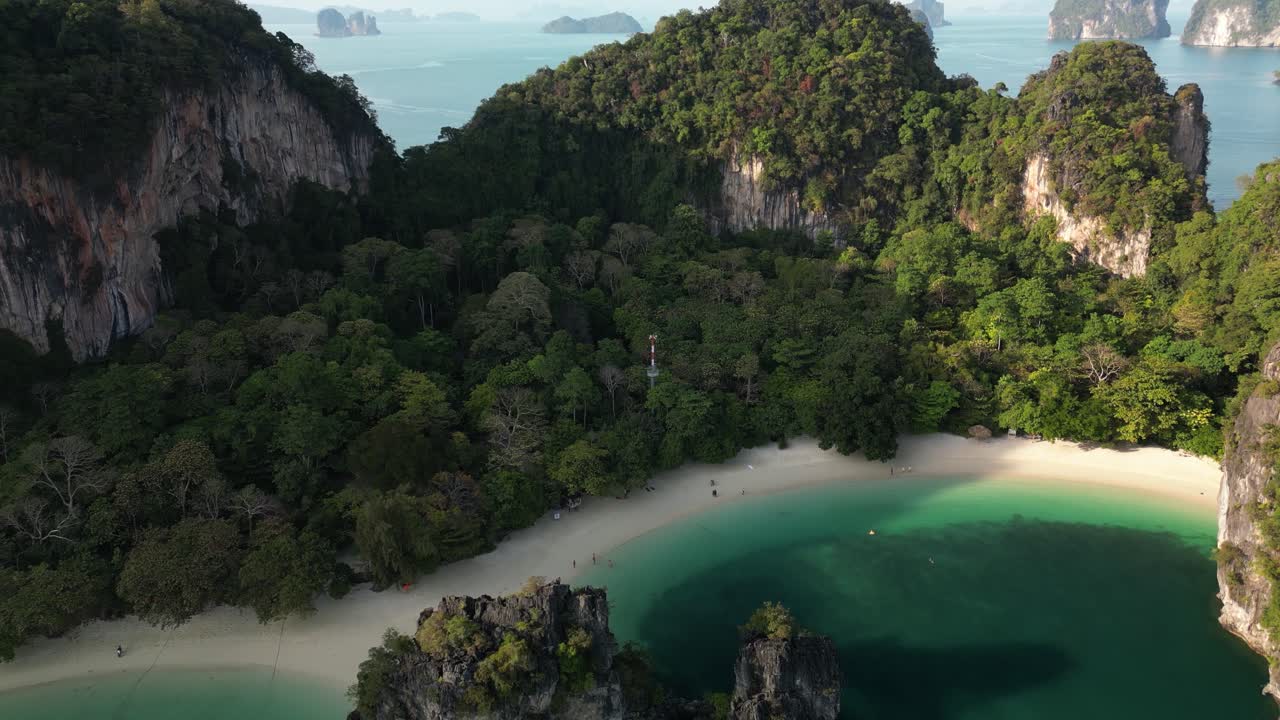 Vista aerea in ascesa dell'isola di Hong a Krabi che mostra scogliere carsiche calcaree coperte di giungla, una spiaggia di sabbia bianca, una laguna color smeraldo e isole sparse nel Mare delle Andamane
