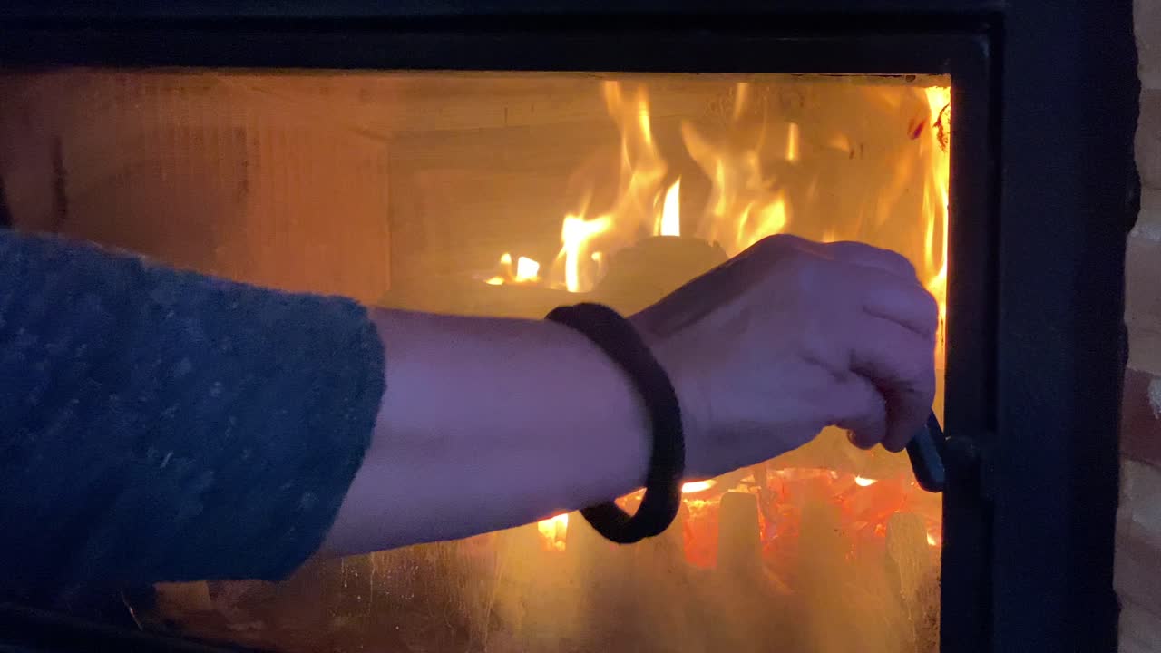 primer plano de una chimenea con la mano de una mujer cerrando el cristal de protección