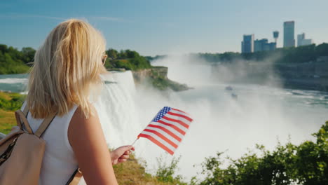 traveling in the usa - a woman with the flag of america in her hand admires niagara falls one of the